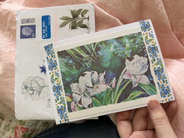 the front of a card with a design of flowers, probably lilies, on top of a mostly hidden envelope.
