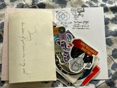 An open greeting card with a pile of stickers and a couple signatures with doodles.